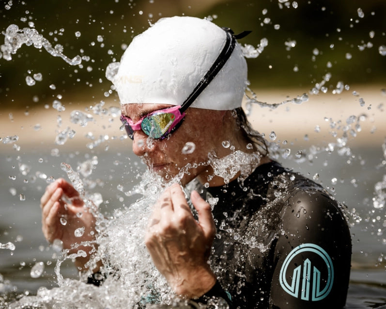 Person in a wetsuit, swim cap and SWANS Ascender goggles splashing water, during a swim event.
