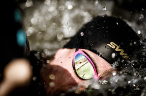 Person swimming underwater with pink swim goggles and black swim cap
